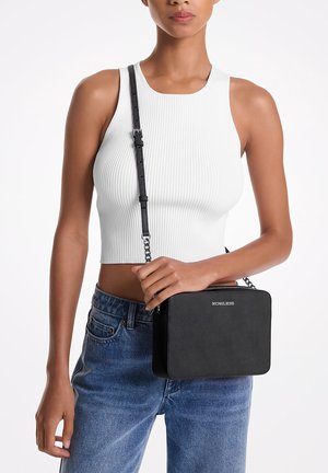 Sort syntetisk crossbody taske med rektangulær form, udstyret med en kædestrop og diskret logo-detalje. Båret sammen med en hvid rippet crop top.