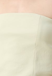 Haut sans bretelles de couleur vert clair, avec une texture lisse et un éclat subtil. Présente un design épuré et ajusté avec des coutures minimales.