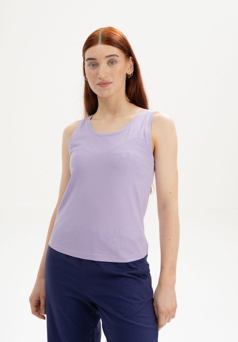 Lila ärmelloses Top mit Rundhalsausschnitt, aus glattem Stoff gefertigt. Es hat ein figurbetontes Design und wird mit navyblauen Hosen kombiniert.