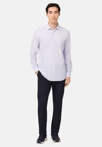 Camicia a maniche lunghe di un azzurro chiaro con colletto, abbinata a pantaloni scuri e sneakers marine. Tessuto morbido con un motivo sottile.
