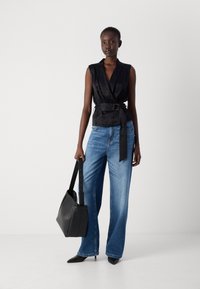 Black satin wrap top with a belted waist, paired with light blue wide-leg jeans, and black pointed-toe heels, holding a black shoulder bag.