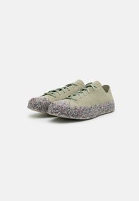 Baskets en tissu vert clair avec une surface texturée, dotées d'une semelle en caoutchouc multicolore à paillettes et de lacets plats assortis.