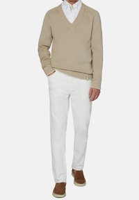 Beige neulepaita V-kaula-aukkolla, yhdistettynä valkoisiin housuihin ja ruskeisiin mokkanahkakenkiin. Hihansuissa ja helmassa resorit, alla kerroksellinen valkoinen paita.