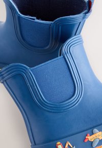 Bottes de pluie en caoutchouc bleues pour enfants avec panneaux latéraux élastiques et décorations colorées d'avions et d'engins de construction.