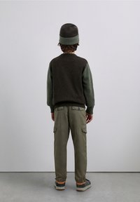 Pull tricoté marron et vert, pantalons cargo et bonnet tricoté ; caractéristiques : poignets côtelés, poches et silhouette décontractée.