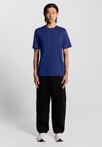 Marineblå kortermet t-skjorte med rund hals, med en liten brodert logo på brystet, kombinert med løse svarte bukser og hvite joggesko.