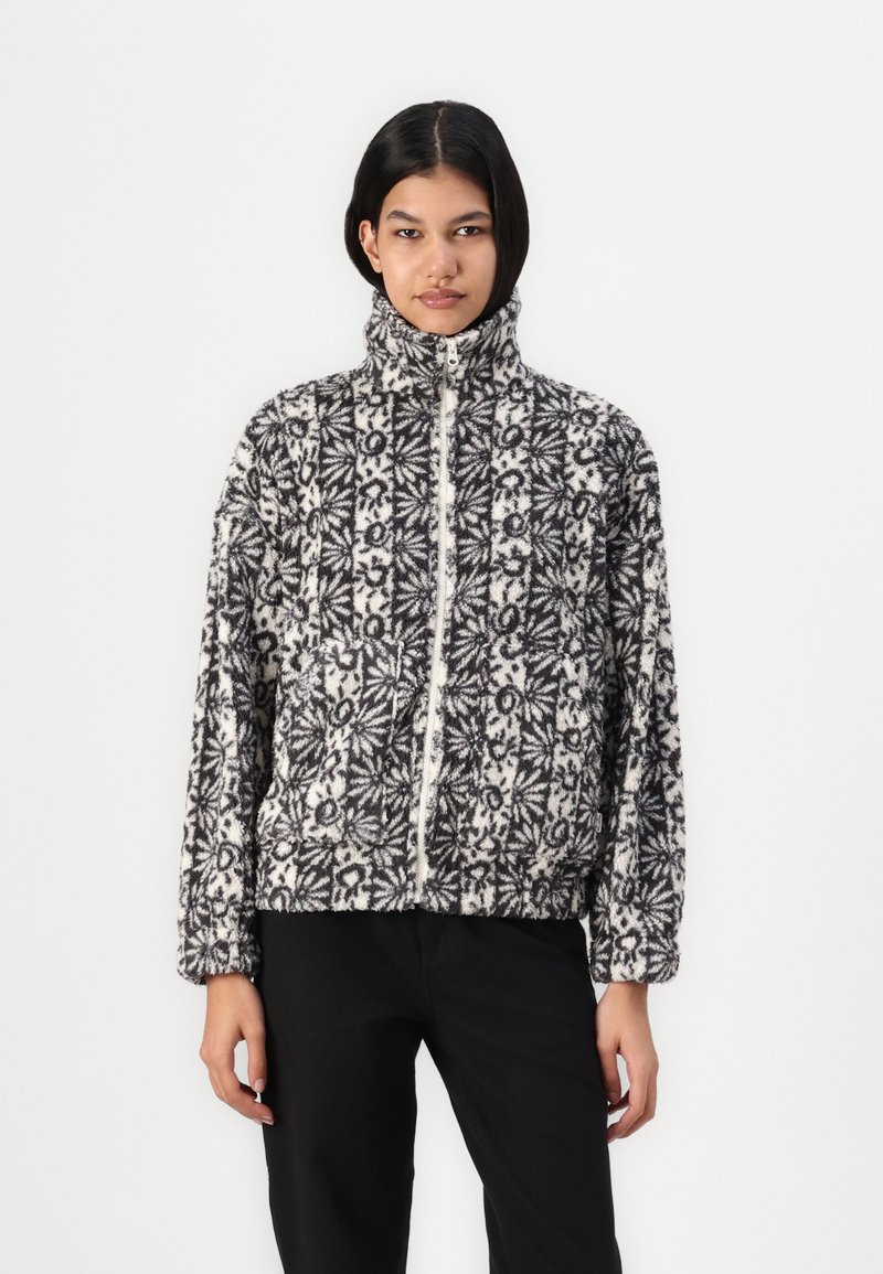 Veste zippée à motifs noir et blanc avec un col montant, fabriquée à partir d'un tissu doux et texturé ; présente des poignets et un ourlet élastiques.