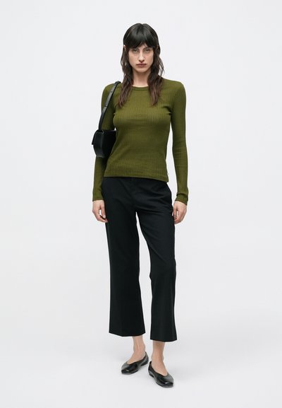 Μακρυμάνικο τοπ σε ελιά πράσινο με ριμπ ύφανση, συνδυασμένο με μαύρο ελαφρώς κοντό παντελόνι και μαύρα μπαλαρίνια. Απλός σχεδιασμός, ελάχιστο μεταλλικό διακοσμητικό, λεία υφή.