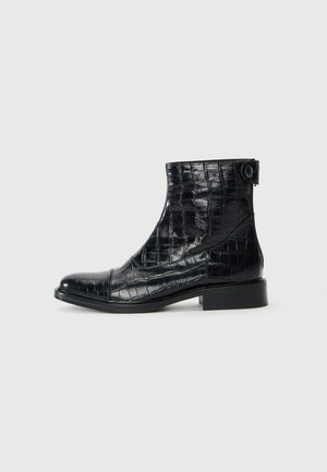 Bottines en cuir noir avec une texture crocodile, bout rond et petit talon carré. Elles disposent d'une fermeture éclair sur le côté et d'un détail en bouton.