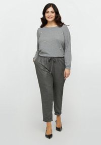 Lichtgrijze longsleeve top met kraalaccenten, gecombineerd met donkergrijze tapering broek met een trekkoord. Zwarte puntige hakken.