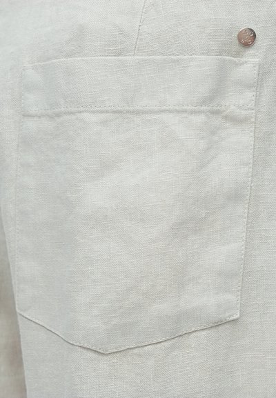 Tissu en lin beige clair avec un détail de poche simple et un bouton argenté en accent, présentant une texture douce et un design minimaliste.