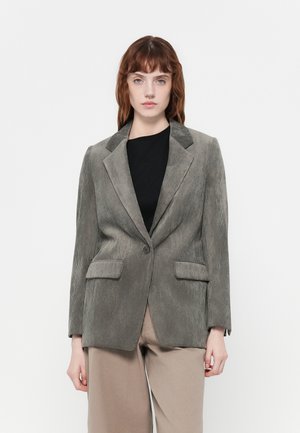 Gray corduroy blazer with structured shoulders, two front pockets, single button closure, and a slightly oversized fit, worn over a black top.
