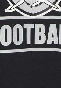 Schwarzes T-Shirt mit fett gedrucktem weißen Text "FUSSBALL." Darüber befindet sich eine Grafik mit gekreuzten sportbezogenen Gegenständen.