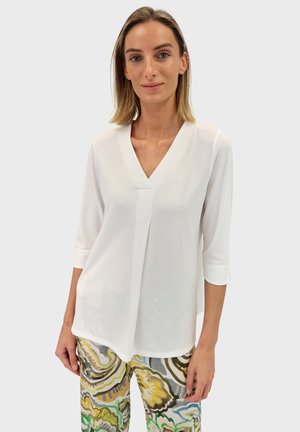 White, lightweight blouse with three-quarter sleeves and a V-neck design. Paired with patterned, multi-colored pants featuring floral motifs.