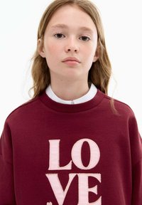 Bordeauxrotes Sweatshirt mit rundem Halsausschnitt, das große, pink gestickte Buchstaben mit der Aufschrift "LOVE" präsentiert. Glatte Textur, lockere Passform und einfaches Design.
