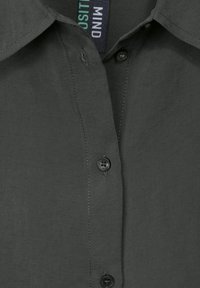 Camicia grigia scura con design a bottone, tessuto morbido e bottoni neri a contrasto sul patta. L'etichetta mostra la dicitura "MIND."