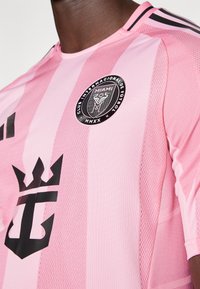 Pink fodboldtrøje med sorte accenter, stribet design, mesh tekstur og cirkulært holdlogo med en krone og "Miami" tekst.