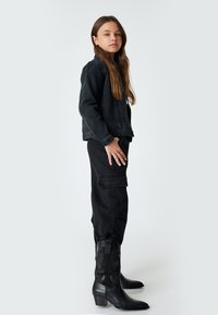 Svart denimjacka med avslappnad passform, matchad med cargobyxor och svarta cowboyboots med präglade detaljer. Jämna texturer genomgående.