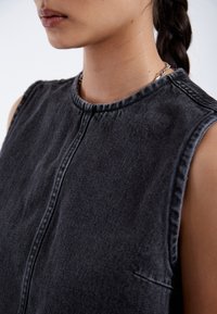 Sleeveless black denim top with a high neckline, visible stitching details, and a front seam. Smooth texture, minimalistic design.