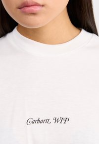 Bílá bavlněná tričko s kulatým výstřihem a černým nápisem "Carhartt WIP" na přední straně, které se vyznačuje hladkou texturou.