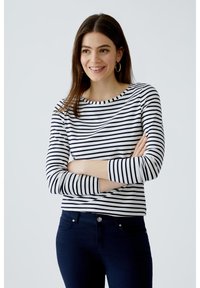 Gestreiftes langärmeliges Oberteil in Blau und Weiß mit Rundhalsausschnitt und schmaler Passform, kombiniert mit dunklen Jeans. Minimalistisches Design, weicher Stoff.