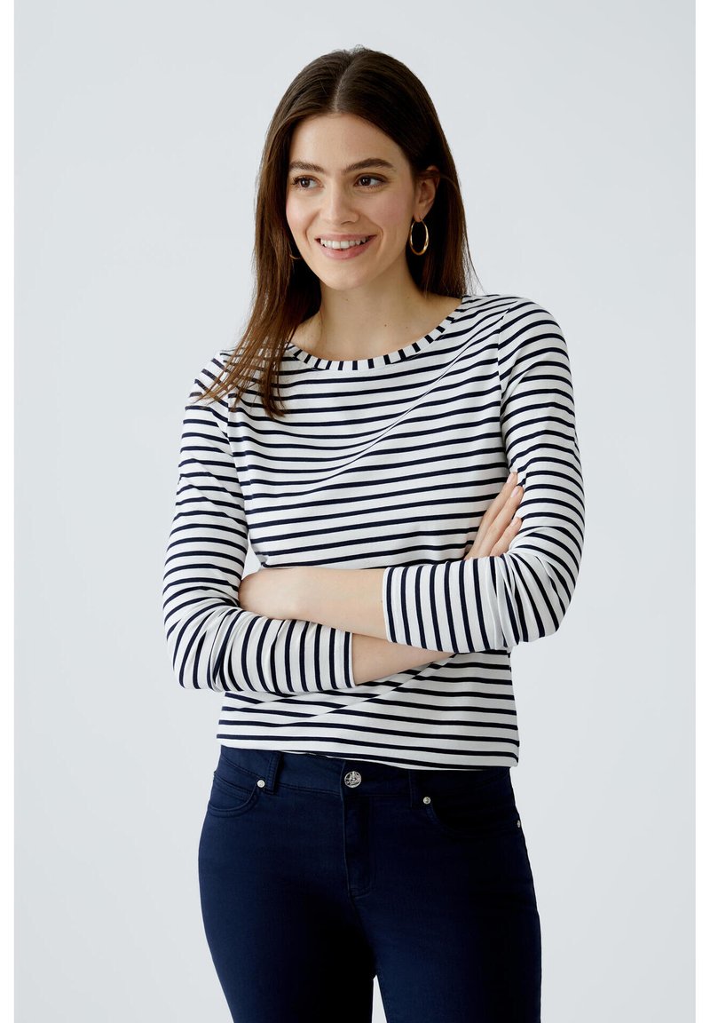 Gestreiftes langärmeliges Oberteil in Blau und Weiß mit Rundhalsausschnitt und schmaler Passform, kombiniert mit dunklen Jeans. Minimalistisches Design, weicher Stoff.