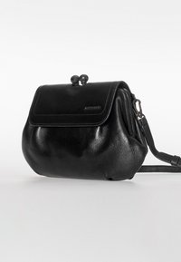 Black leather crossbody bag with round clasp closure and long adjustable strap, featuring subtle embossed brand name on the front flap.