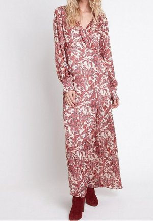 Woman wearing a long-sleeve, ankle-length dress with red floral patterns, paired with red suede ankle boots, standing against a plain background.