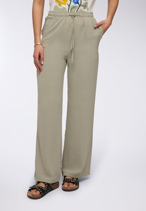 Pantaloni a gamba larga verde chiaro, texture, con vita elastica e cordoncino. Il modello indossa sandali neri con borchie. Due tasche laterali visibili.