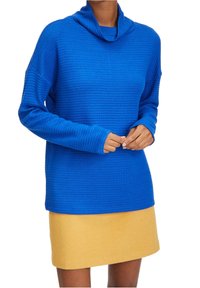 Top azul de cuello vuelto con textura acanalada y hombros caídos, combinado con una falda amarilla. Ambas prendas están hechas de materiales suaves y tejidos.