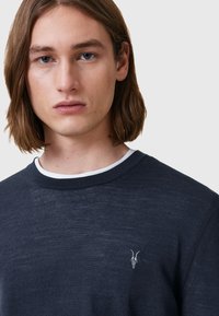 Navyblauer Pullover mit Rundhalsausschnitt, der eine dezente dunklere Struktur sowie ein kleines gesticktes Ziegelschädel-Logo auf der linken Brust aufweist.