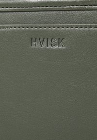 Groen leren product met een geperst "HVISK" logo, een gladde textuur en gestikte details. Compacter ontwerp met een strakke afwerking.