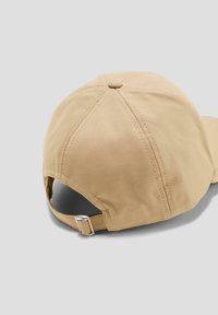 Beige pet met een zachte stof, zespanelen ontwerp, gestructureerde vorm en een verstelbare riem aan de achterkant met een metalen gesp.