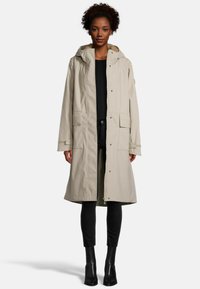 Beige waterdichte jas met een capuchon, voorrits en drukknoopsluiting, twee grote voorzakken en een zachte voering.