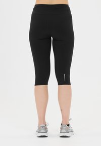 Mustat capri leggingsit, joissa on korkea vyötärö ja tyylikäs muotoilu. Niissä on heijastavat yksityiskohdat helman lähellä ja sileä, joustava materiaali.