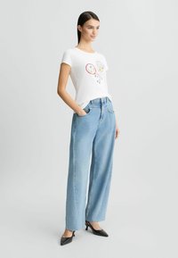 T-shirt en coton blanc avec un graphique coloré de raquette de tennis ; jeans taille haute bleu clair à jambes larges ; chaussures noires à bout pointu. Tenue simple et décontractée.