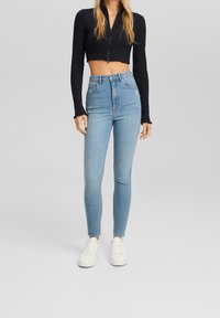 Jeans de mezclilla claros de tiro alto con un ajuste slim, que presentan acentos desgastados y una textura suave, combinados con zapatillas blancas.