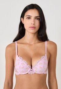 Light pink bra with floral embroidery, lace detailing along the edges, adjustable straps, and a small bow at the center.