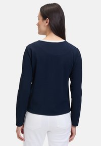 Haut à manches longues bleu marine avec un motif texturé et un col blanc. Le dos présente un ourlet arrondi et des manches ajustées.