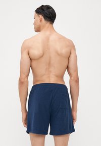 Námořnické modré bavlněné šortky s elastickým pasem, se zadní kapsou a měkkou texturovanou tkaninou. Model zobrazen zezadu.