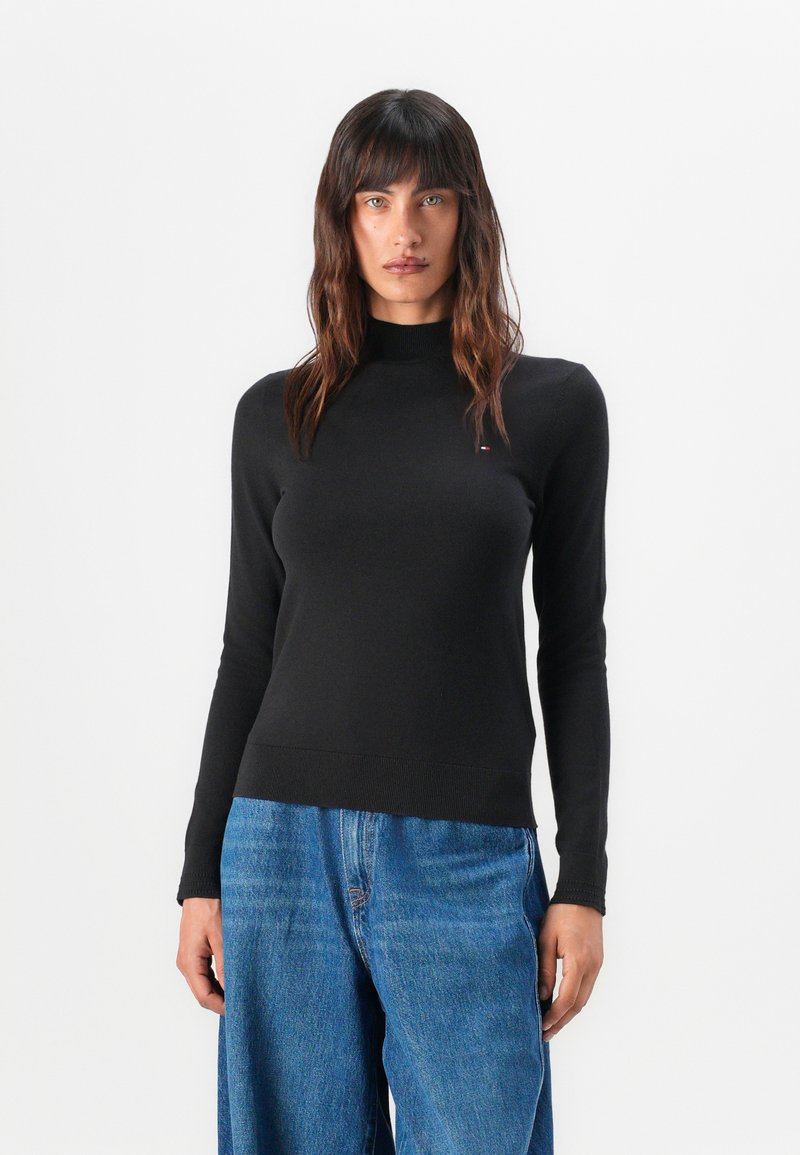 Maglione nero a manica lunga con collo alto, realizzato in un tessuto liscio. Caratterizzato da un design aderente e dettagli a coste visibili sull'orlo.