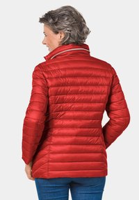 Doudoune rouge avec un design matelassé horizontal, col haut et matériau léger. Présente une coupe ajustée et une texture lisse.