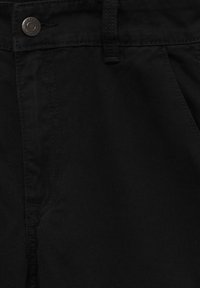 Zwarte denimbroek met een gladde textuur, voorzien van een tailleband met riemlussen en een bronzen knoopdetail aan de voorkant.