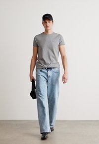 Γκρι κοντομάνικο T-shirt, ξεθοριασμένα μπλε φαρδιά τζιν, μαύρο καπέλο μπέιζμπολ και μαύρα παπούτσια. Το μοντέλο κρατά μια μαύρη τσάντα στο αριστερό χέρι.