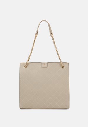 Beżowa pikowana torba tote o wyraźnym kształcie, ze złotymi łańcuszkami nałożonymi na ramię oraz plakietką z logo. Gładka faktura oraz wzór w diamenty na całej powierzchni.