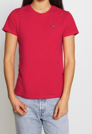 Camiseta roja de algodón con cuello redondo y mangas cortas, que presenta un pequeño logo de Levi's en el pecho izquierdo. Combinada con vaqueros de lavado claro.