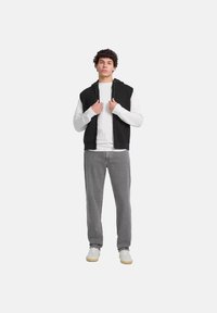 Chaleco negro con capucha sobre una camiseta de manga larga blanca, pantalones grises y zapatillas blancas. Estilo casual con cremallera y bolsillos frontales.