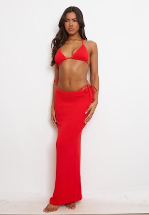 Rode gebreide bikini-top met driehoekige cups en verstelbare banden, gecombineerd met een lange, aansluitende rode gebreide maxi-rok met zijstrikjes.