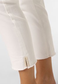 Vita beskurna jeans med rå nederkant, med ett snittdetalj vid vristen och kontrasterande sömmar. Tillverkade av mjuk, medeltjock denim.