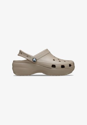 Beige Clog mit geschlossenem Rücken aus strapazierfähigem Material, ausgestattet mit Belüftungsöffnungen, einem strukturierten Band und einem runden Logo-Akzent an der Seite.